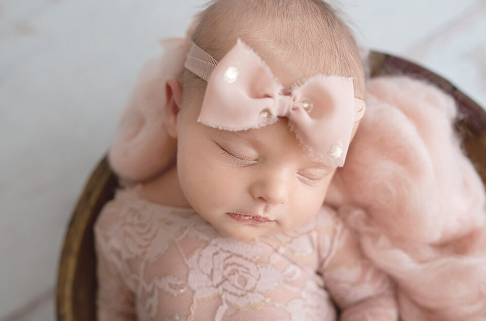 Newborn Baby with Pink Bow in a Wooden Bowl